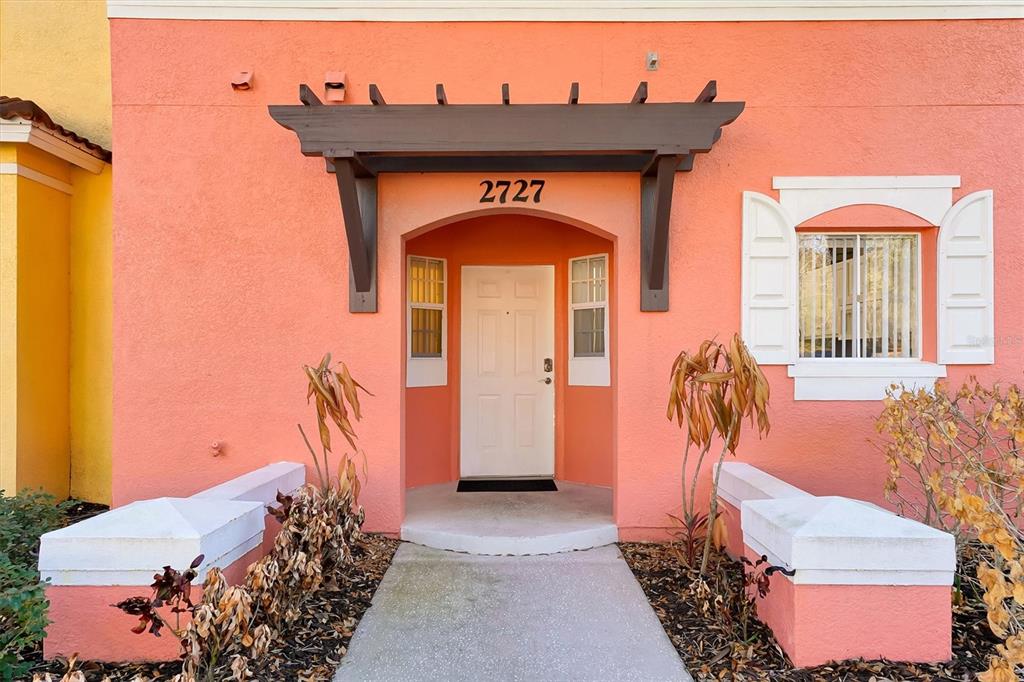 The exterior of a peach-colored home features a brown pergola over the front entrance — 2727 SUN KEY PLACE, KISSIMMEE, FL