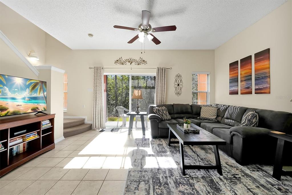 A living room features a dark sectional sofa, a coffee table, and a sliding glass door — 2727 SUN KEY PLACE, KISSIMMEE, FL