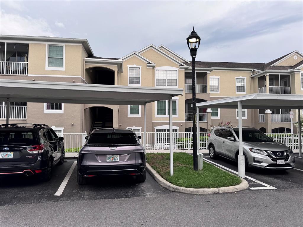 A three-story apartment building exterior features covered parking spaces and three parked vehicles — 586 BRANTLEY TERRACE WAY UNIT 301, ALTAMONTE SPRINGS, FL