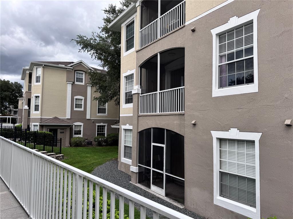 The exterior of a multi-story apartment building features tan stucco walls, white trim, and screened balconies — 586 BRANTLEY TERRACE WAY UNIT 301, ALTAMONTE SPRINGS, FL