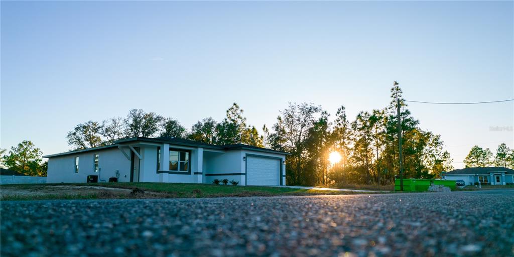 A single-story white house with a garage sits near a road at sunset — 10034 N DARWIN WAY, CITRUS SPRINGS, FL