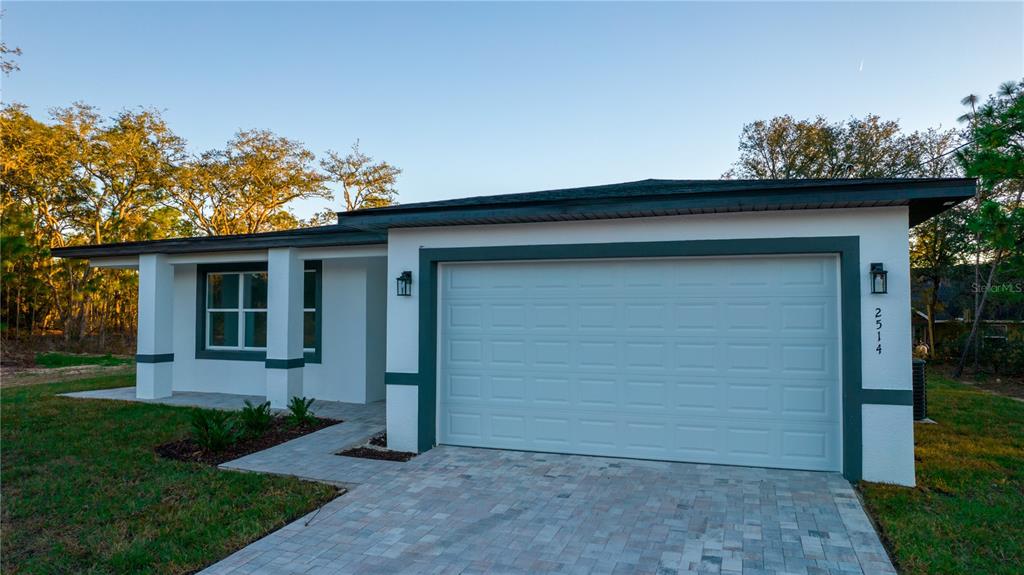 A single-story house exterior features a white stucco facade, dark trim, and a paved driveway — 10034 N DARWIN WAY, CITRUS SPRINGS, FL