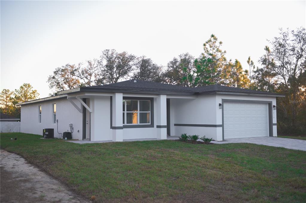 A single-story house with white stucco walls, dark trim, and an attached two-car garage — 10034 N DARWIN WAY, CITRUS SPRINGS, FL