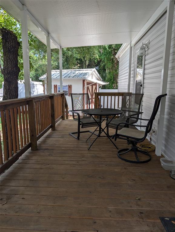 A covered wooden deck features a small round table and three chairs outside a home — 25364 NE 139TH LOOP, FORT MC COY, FL