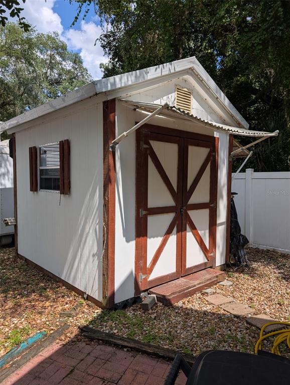 A white wooden storage shed with brown trim and double doors sits on a gravel yard — 25364 NE 139TH LOOP, FORT MC COY, FL