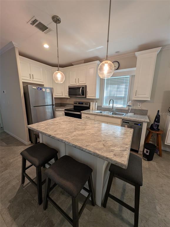 A kitchen features white cabinets, stainless steel appliances, a marble-patterned island, and three bar stools — 25364 NE 139TH LOOP, FORT MC COY, FL