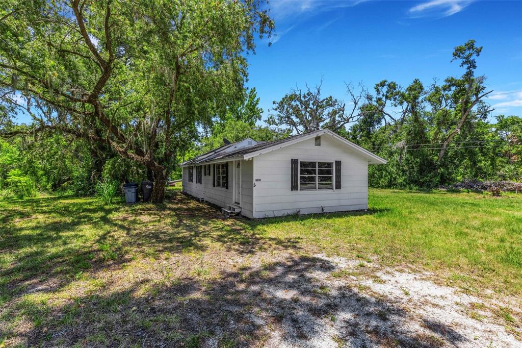 A white, single-story house sits on a grassy lot surrounded by large, leafy trees — 8010 BROWER DRIVE, BRADENTON, FL