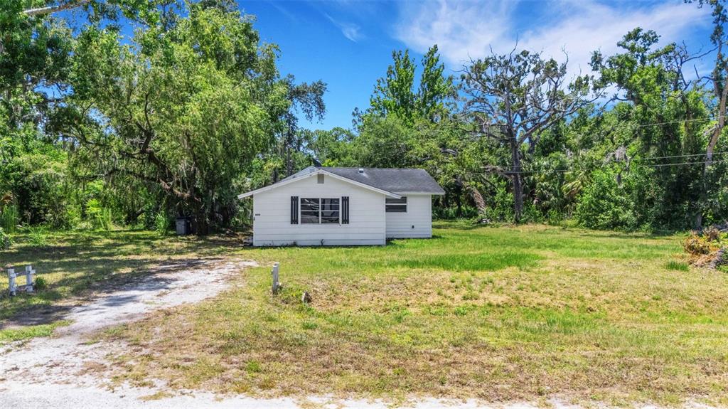 A small, white, single-story house sits on a grassy lot surrounded by mature trees — 8010 BROWER DRIVE, BRADENTON, FL
