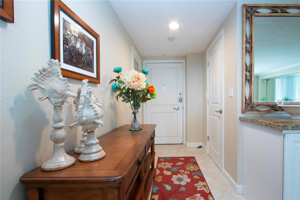 A hallway features a wooden console table, floral runner, and a mirror on the wall — 1212 BENJAMIN FRANKLIN DRIVE UNIT 607, SARASOTA, FL