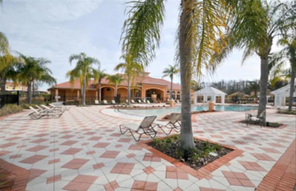 A swimming pool area with lounge chairs, palm trees, and a clubhouse in the background — 890 MARCELLO BOULEVARD, KISSIMMEE, FL