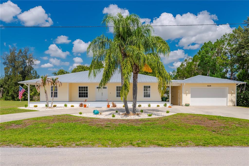 A yellow single-story house with a metal roof, front porch, and attached garage — 569 RIO VISTA AVENUE, PUNTA GORDA, FL