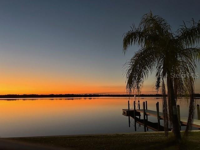 A palm tree stands beside a wooden dock overlooking a lake at sunset — 569 RIO VISTA AVENUE, PUNTA GORDA, FL