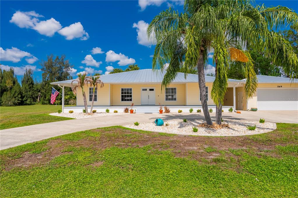 A yellow single-story house with a metal roof and a palm tree in the yard — 569 RIO VISTA AVENUE, PUNTA GORDA, FL