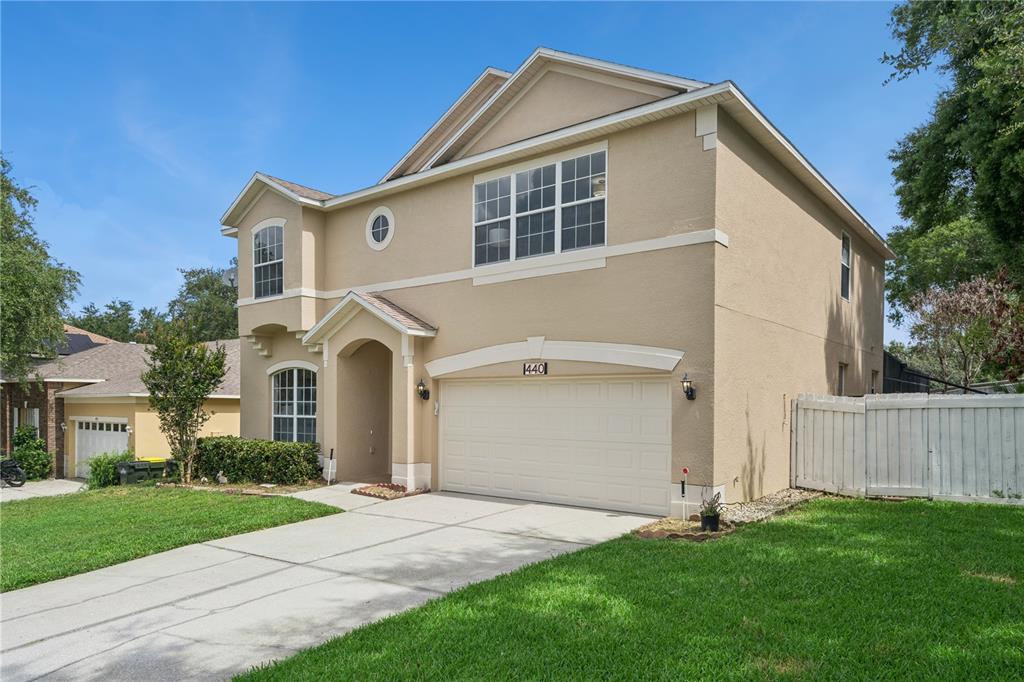 A two-story suburban house with a beige stucco exterior, a two-car garage, and a driveway — 440 ROB ROY DRIVE, CLERMONT, FL