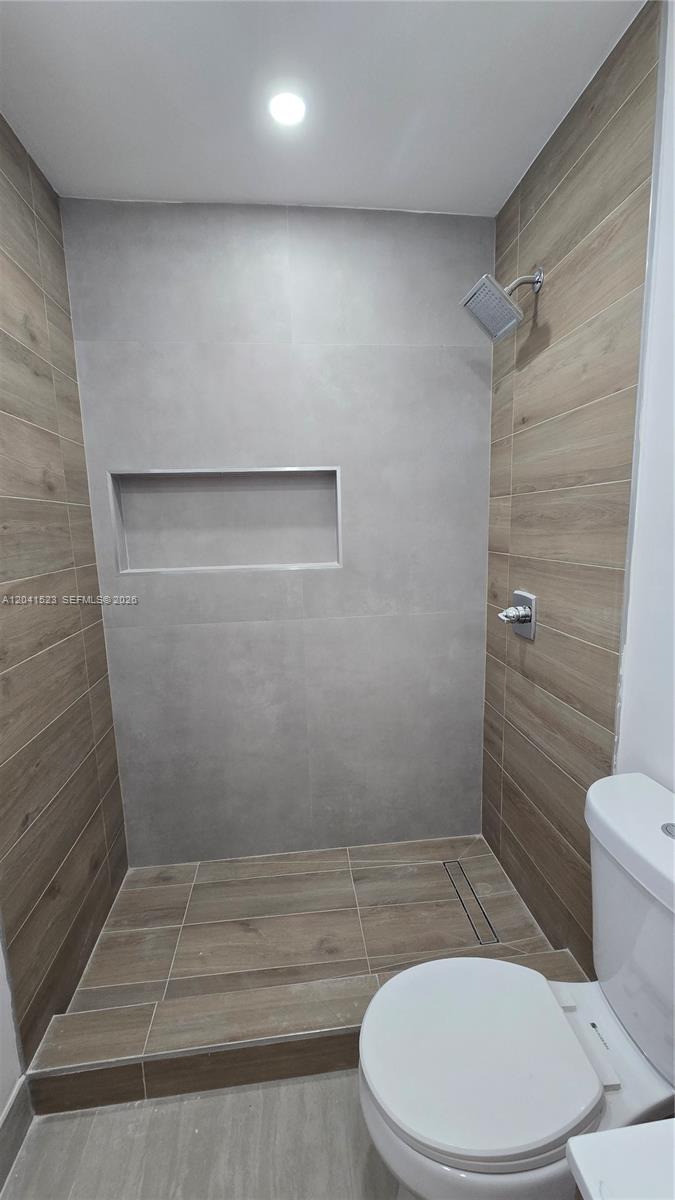 A bathroom features a walk-in shower with wood-look tile, gray wall tiles, and a niche — MIAMI, FL