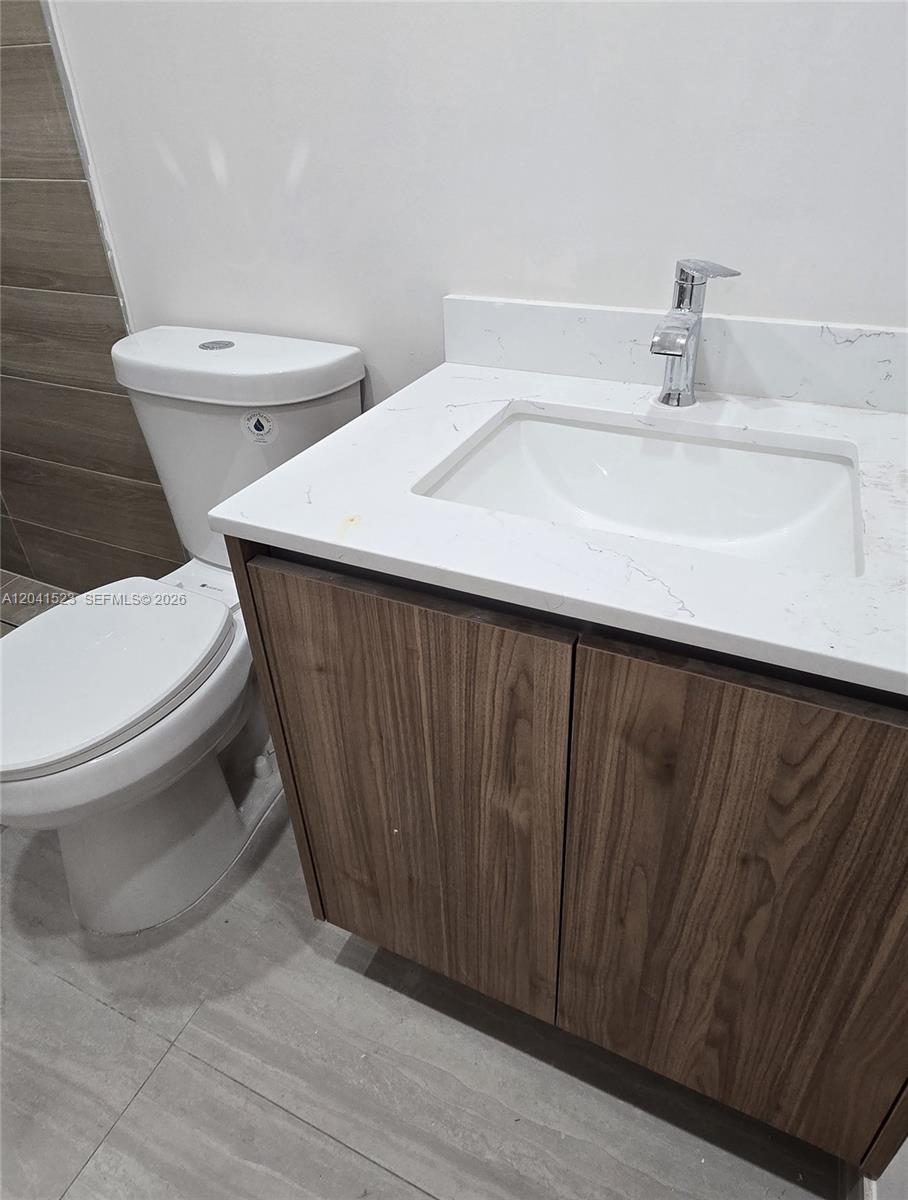 A bathroom features a wood-grain vanity with a white countertop and a white toilet — MIAMI, FL