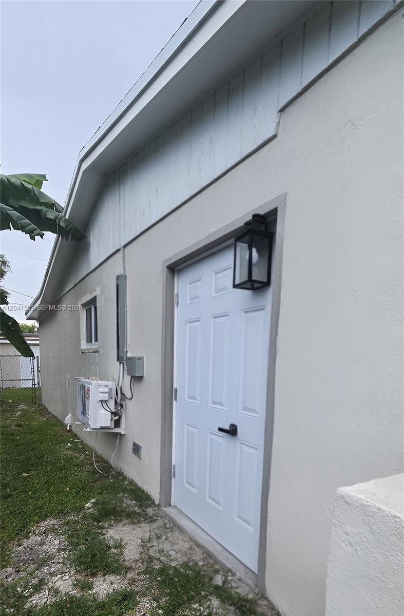 The exterior of a house features a white door, a wall-mounted AC unit, and siding — MIAMI, FL