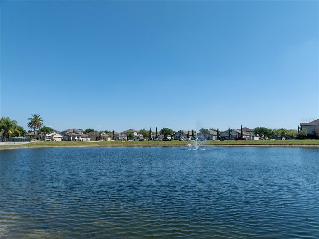 A view of a neighborhood pond with a fountain and houses in the background — 1110 UMBRIA LANE, ST CLOUD, FL