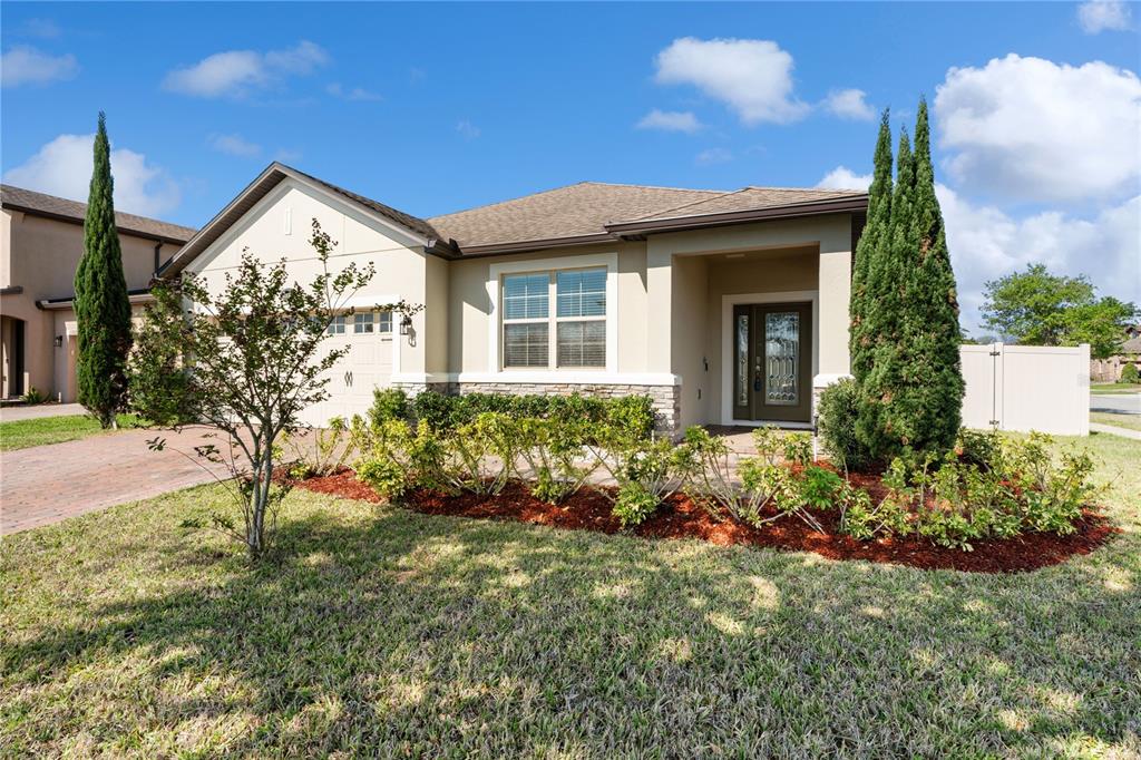 A single-story house with a beige stucco exterior, stone accents, and a front-facing garage — 1110 UMBRIA LANE, ST CLOUD, FL
