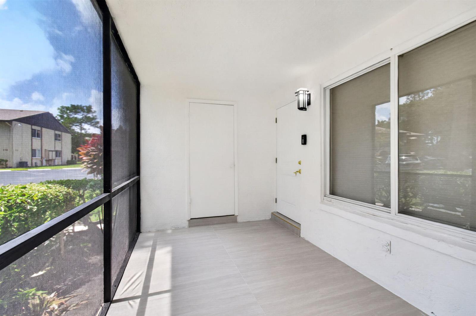 A screened-in porch with light-colored tile flooring, a white entry door, and a large window — 314 Pine Ridge Circle # A1, FL 33463, FL
