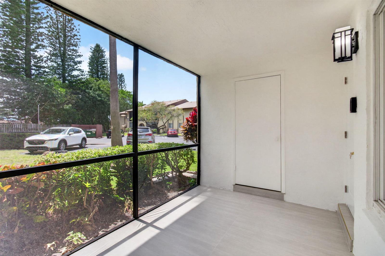 A screened-in porch features light-colored tile flooring, a white door, and a view of parking — 314 Pine Ridge Circle # A1, FL 33463, FL