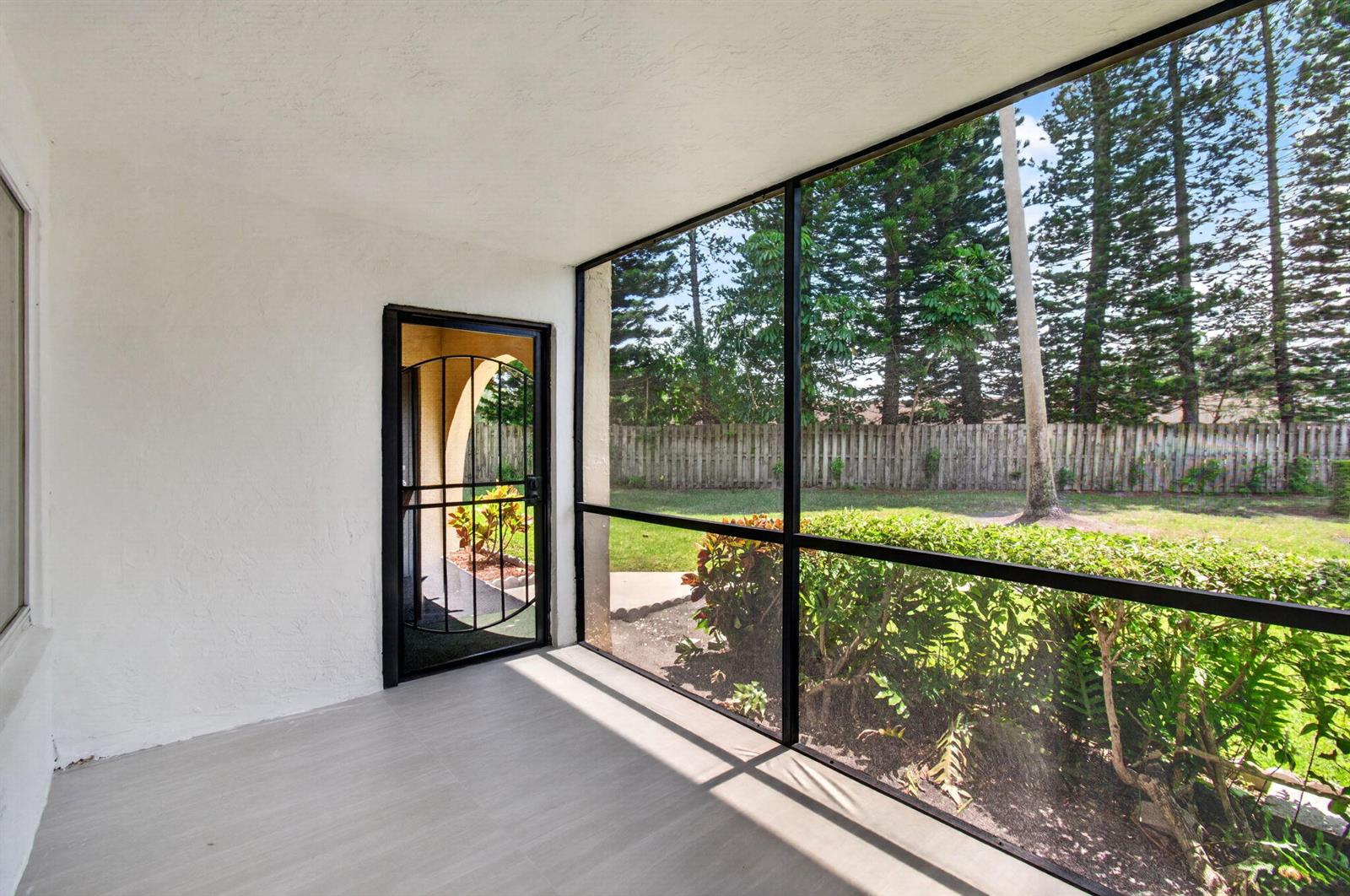A screened-in porch with light-colored flooring, white walls, and a view of a backyard — 314 Pine Ridge Circle # A1, FL 33463, FL