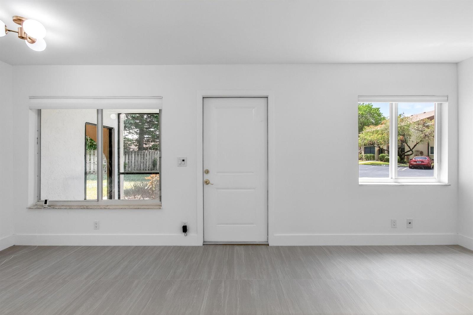 A bright room features white walls, light wood-look flooring, a central door, and two windows — 314 Pine Ridge Circle # A1, FL 33463, FL
