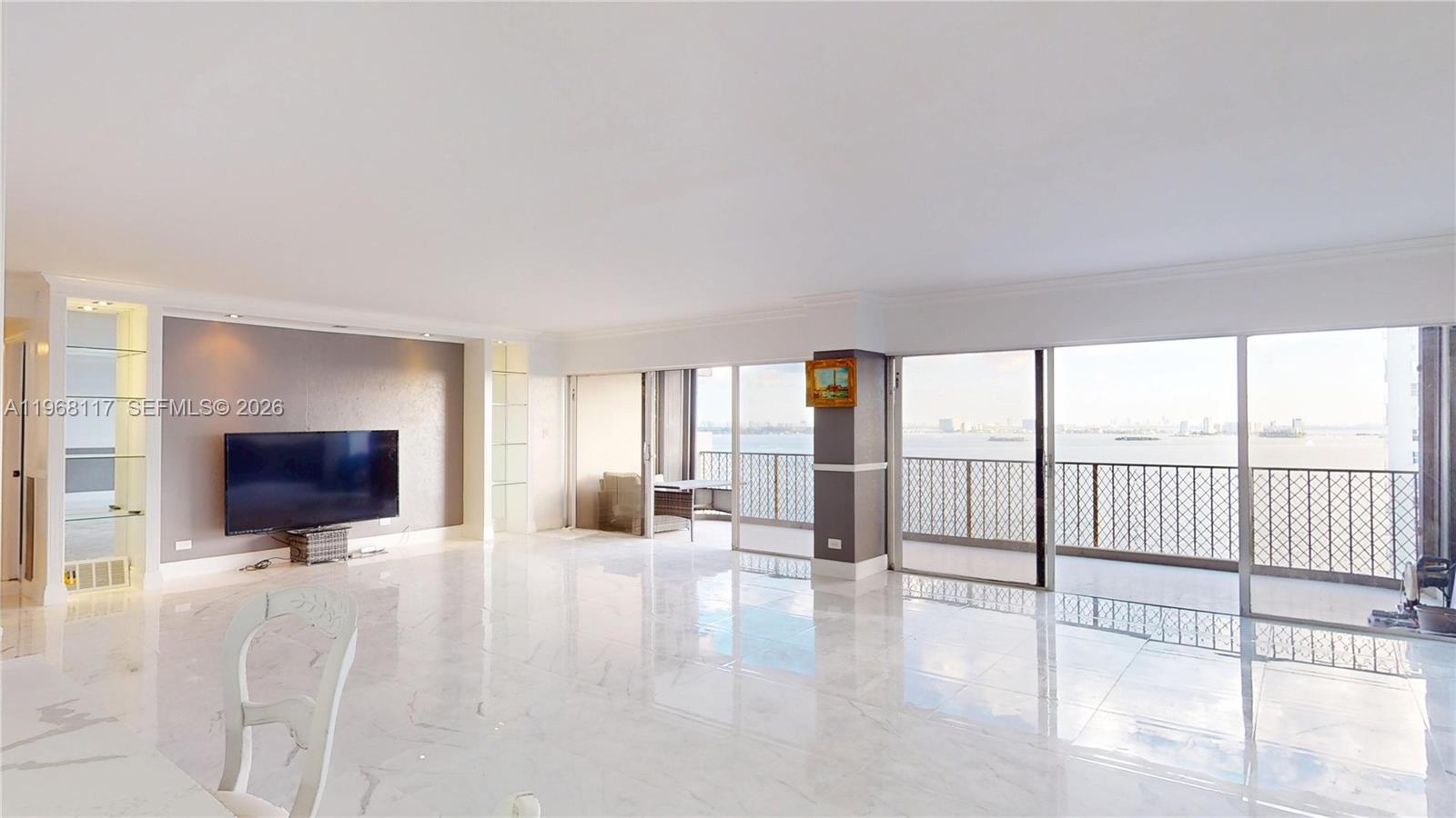 A spacious living room features white marble floors, a wall-mounted television, and a large balcony — 1800 NE 114th St # 1705, Miami FL 33181, MIAMI, FL