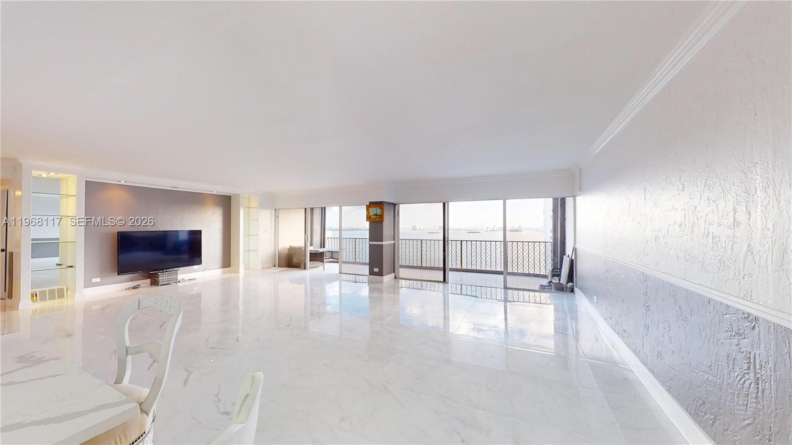 A spacious living room features white marble floors, a wall-mounted television, and a balcony view — 1800 NE 114th St # 1705, Miami FL 33181, MIAMI, FL