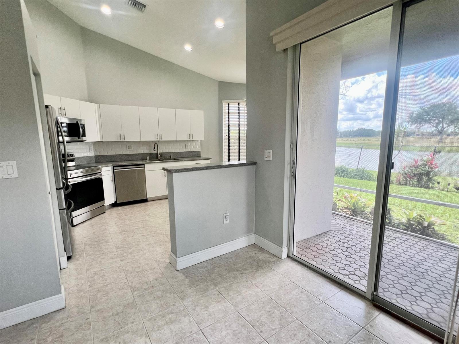 A kitchen with white cabinets and stainless steel appliances opens to a patio with water views — 7801 S Aragon Boulevard # 4, Sunrise FL 33322, SUNRISE, FL