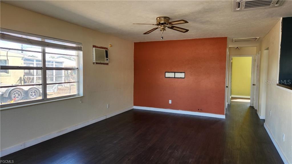 A living room features dark wood-look flooring, a ceiling fan, and a rust-colored accent wall — 1169 CHEROKEE AVENUE, LEHIGH ACRES, FL