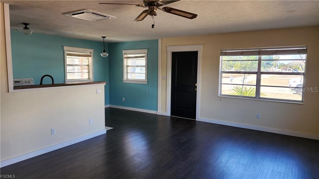 A living room features dark wood-look flooring, light yellow walls, blue accent walls, and a ceiling fan — 1169 CHEROKEE AVENUE, LEHIGH ACRES, FL