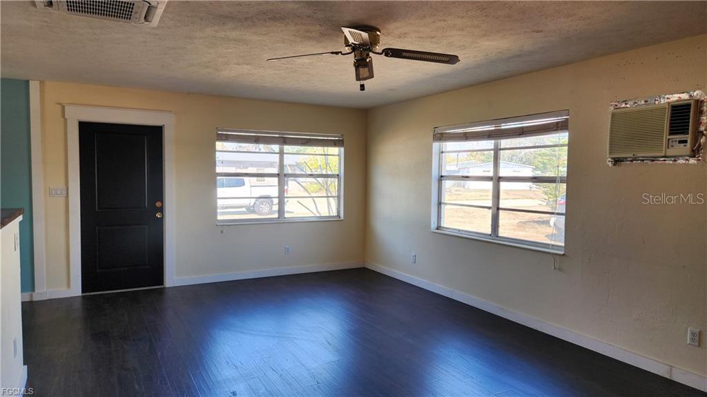A living room with dark wood floors, light walls, a ceiling fan, and two windows — 1169 CHEROKEE AVENUE, LEHIGH ACRES, FL