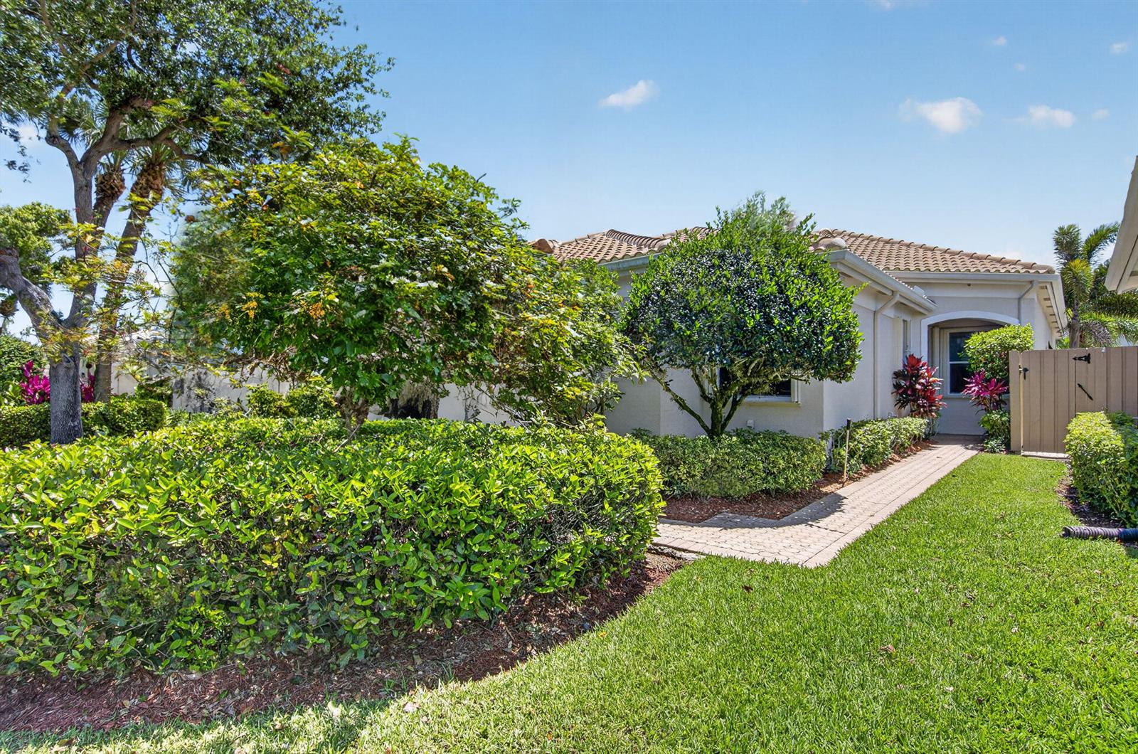 A paved walkway leads to the entrance of a house surrounded by lush green landscaping — 2408 NW 67th Street, Boca Raton FL 33496, BOCA RATON, FL