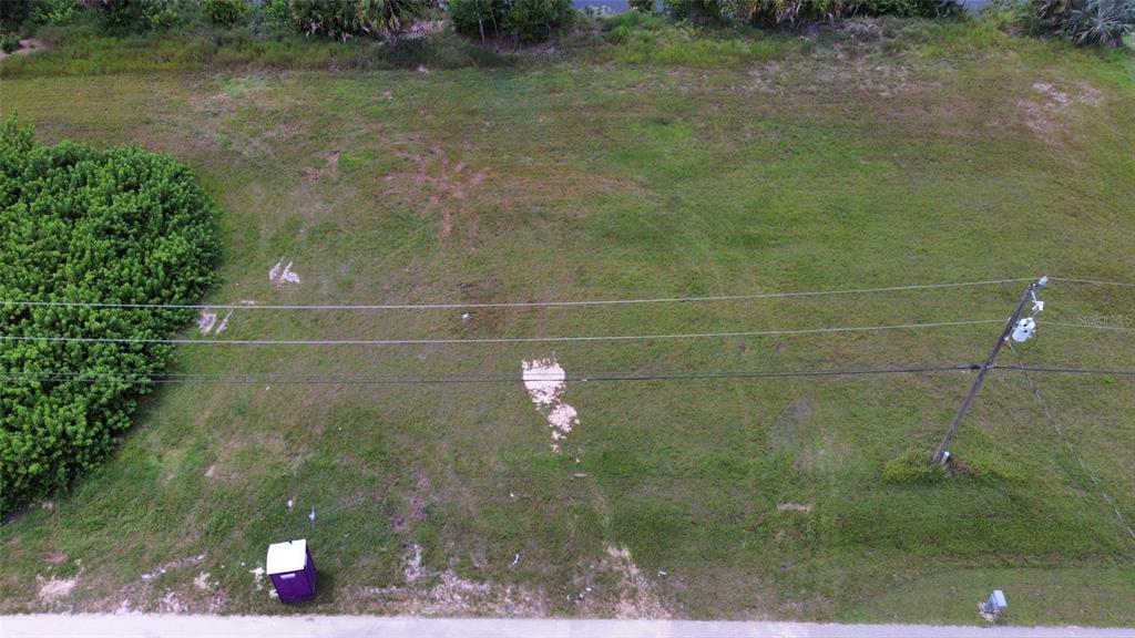An aerial view shows a vacant, grassy lot with a portable toilet and utility pole — 4140 NE 21ST PLACE, CAPE CORAL, FL