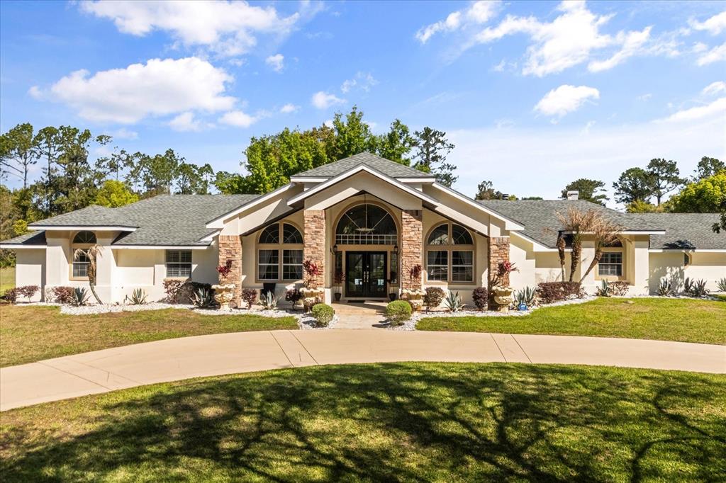 A single-story house with a stone-accented entryway and a curved driveway under a blue sky — 1856 ALAQUA DRIVE, LONGWOOD, FL