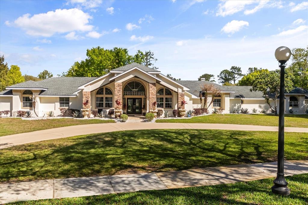 A single-story house with a stone-accented entryway and a curved driveway under a blue sky — 1856 ALAQUA DRIVE, LONGWOOD, FL