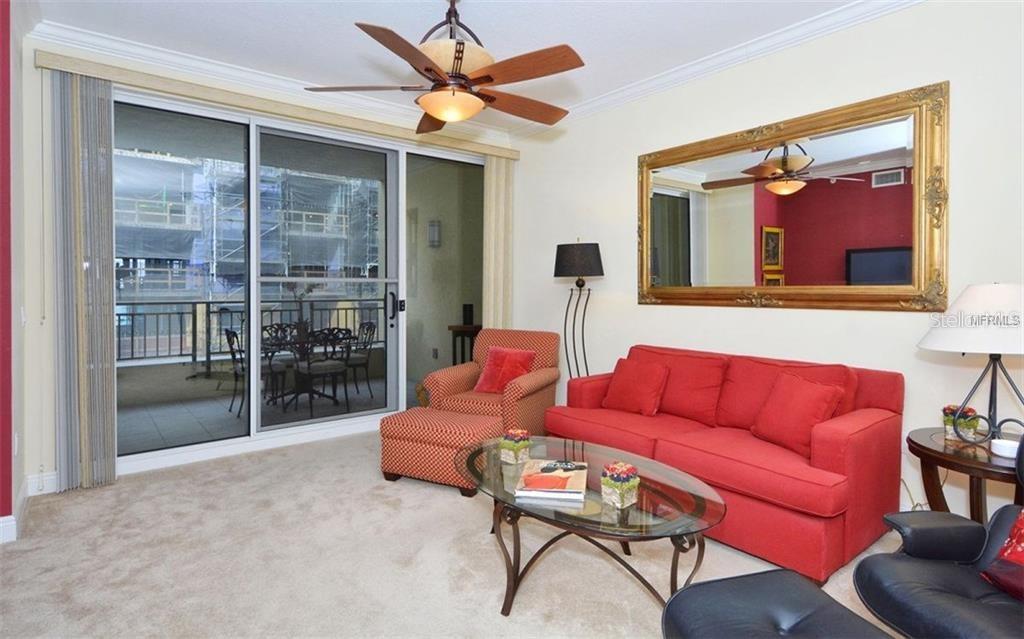 A living room features a red sofa, patterned armchair, glass coffee table, and sliding glass doors — 100 CENTRAL AVENUE UNIT 620, SARASOTA, FL