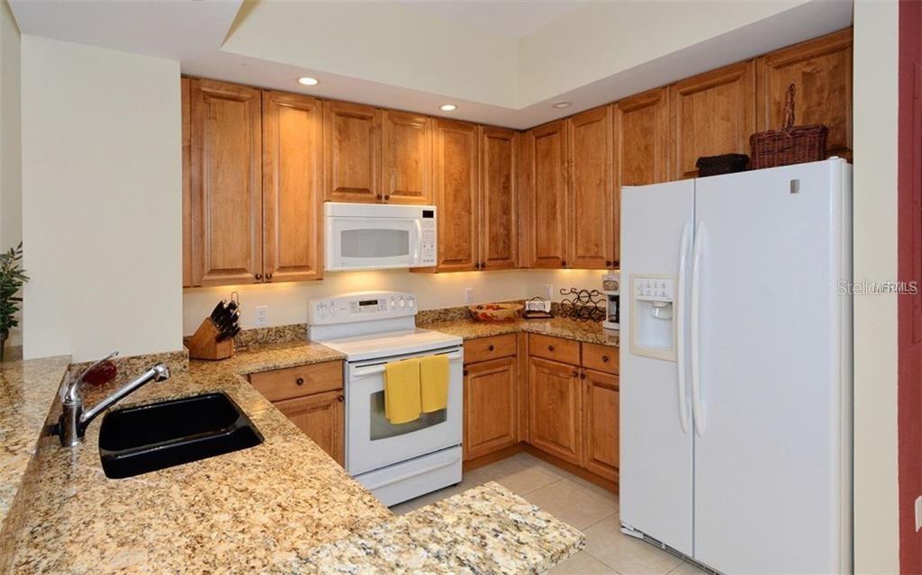 A kitchen with wood cabinets, granite countertops, a white refrigerator, and a black sink — 100 CENTRAL AVENUE UNIT 620, SARASOTA, FL