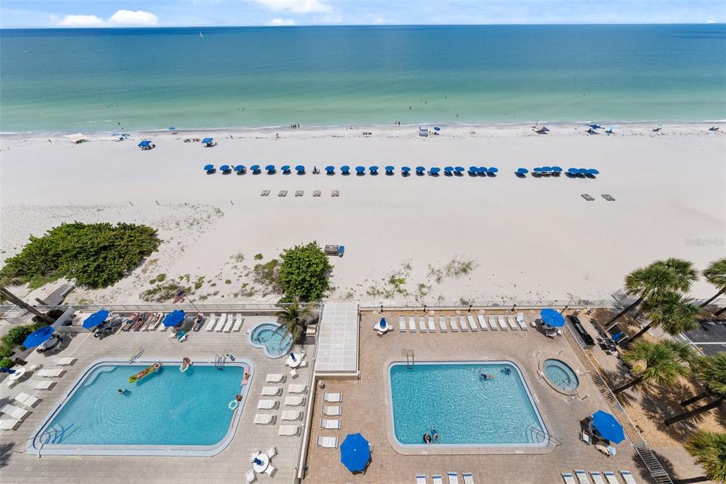 An aerial view shows two swimming pools and a hot tub overlooking a sandy beach — 20002 GULF BOULEVARD UNIT 2, INDIAN SHORES, FL