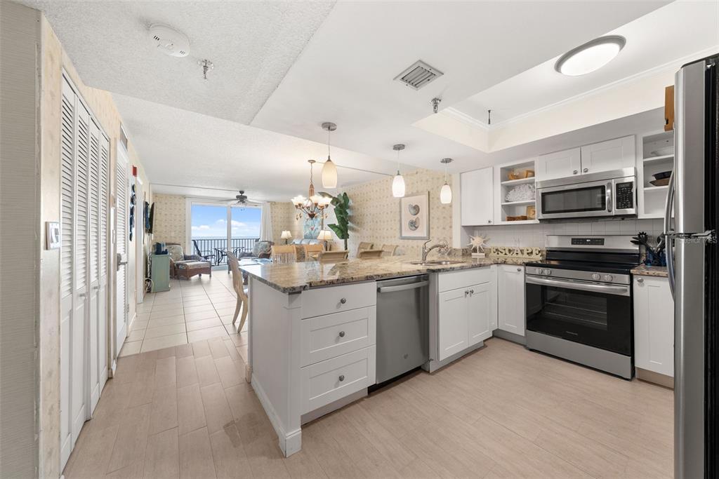 A kitchen with white cabinets, granite countertops, and stainless steel appliances opens to a living area — 20002 GULF BOULEVARD UNIT 2, INDIAN SHORES, FL