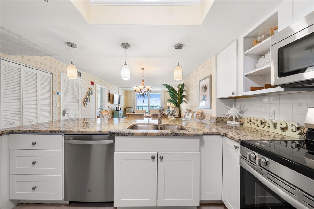 A kitchen with white cabinets, granite countertops, and stainless steel appliances overlooks a living area — 20002 GULF BOULEVARD UNIT 2, INDIAN SHORES, FL
