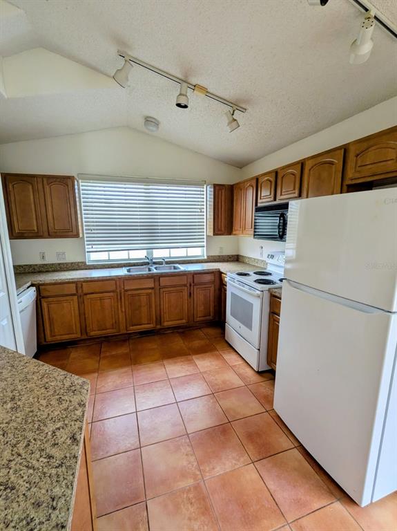 A kitchen features wooden cabinets, tile flooring, white appliances, and track lighting — 334 LADY DIANA DRIVE, DAVENPORT, FL