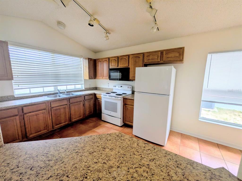 A kitchen features wood cabinets, granite countertops, a white refrigerator, and a white stove — 334 LADY DIANA DRIVE, DAVENPORT, FL
