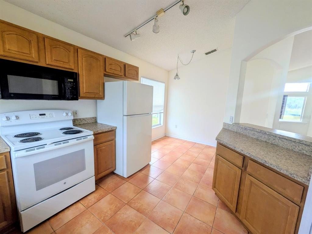 A kitchen with wood cabinets, white appliances, granite countertops, and orange tile flooring — 334 LADY DIANA DRIVE, DAVENPORT, FL