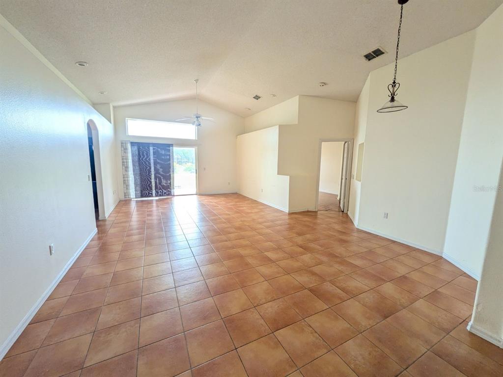 An open living area features vaulted ceilings, tan tile flooring, and a sliding glass door — 334 LADY DIANA DRIVE, DAVENPORT, FL