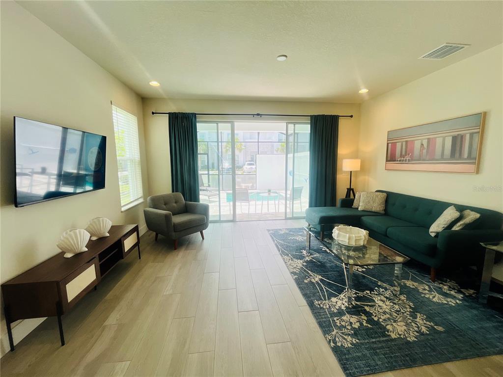 A living room features a teal sectional sofa, a gray armchair, and a glass coffee table — 1399 PEACEFUL NATURE WAY, CLERMONT, FL