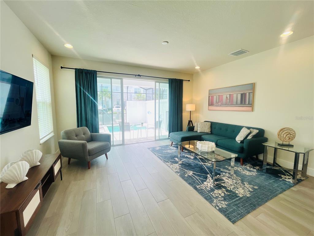 A living room features a teal sectional sofa, gray armchair, and sliding doors to a pool — 1399 PEACEFUL NATURE WAY, CLERMONT, FL