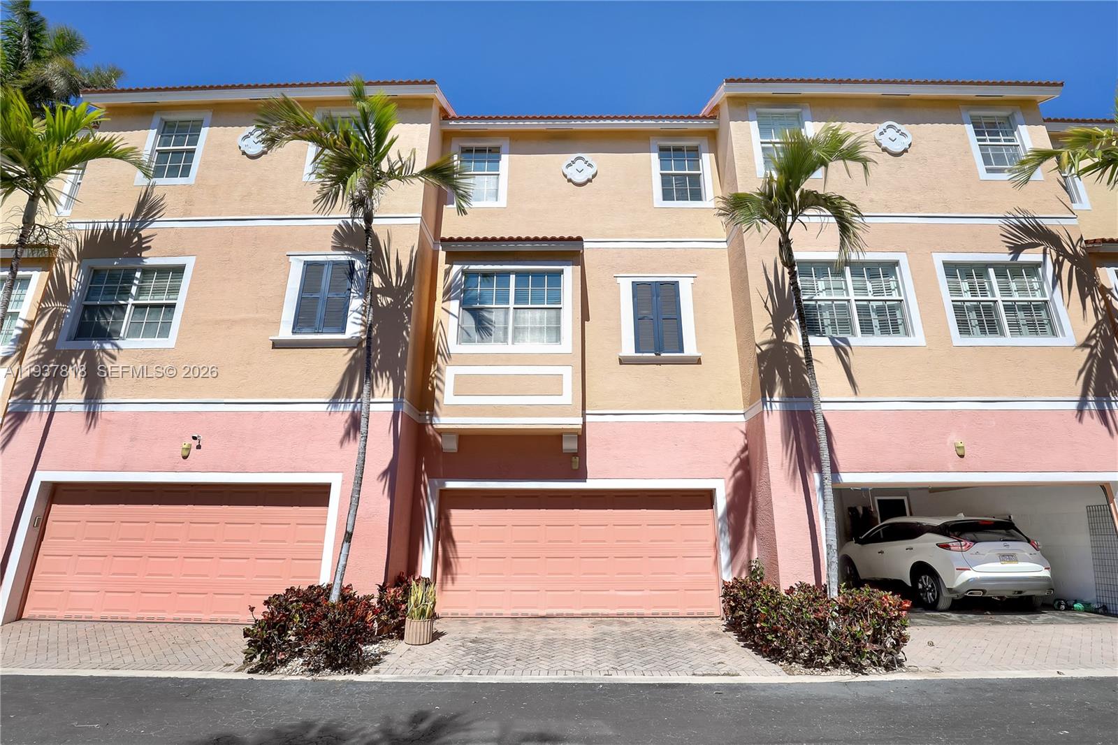The exterior of a multi-story townhouse features peach and pink stucco walls and garage doors — 104 Harbors Way, Boynton Beach FL 33435, BOYNTON BEACH, FL