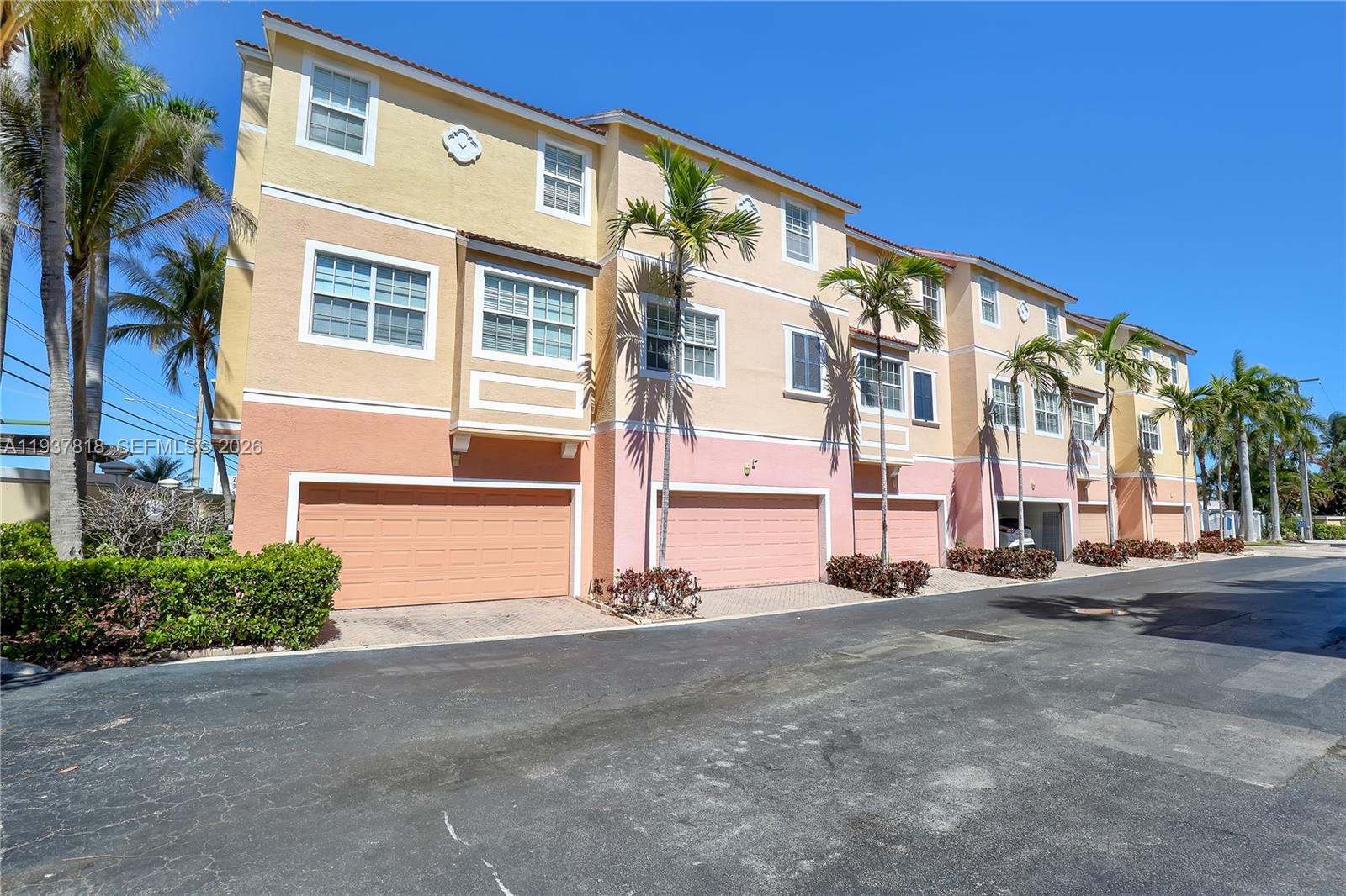 A row of three-story townhomes with pastel-colored stucco facades and attached garages — 104 Harbors Way, Boynton Beach FL 33435, BOYNTON BEACH, FL